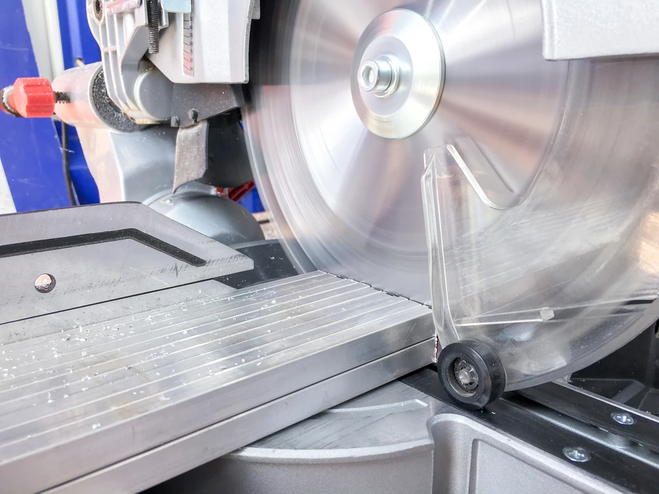 Atelier industriel intérieur avec opérateur manipulant une scie à ruban métallique en fonctionnement