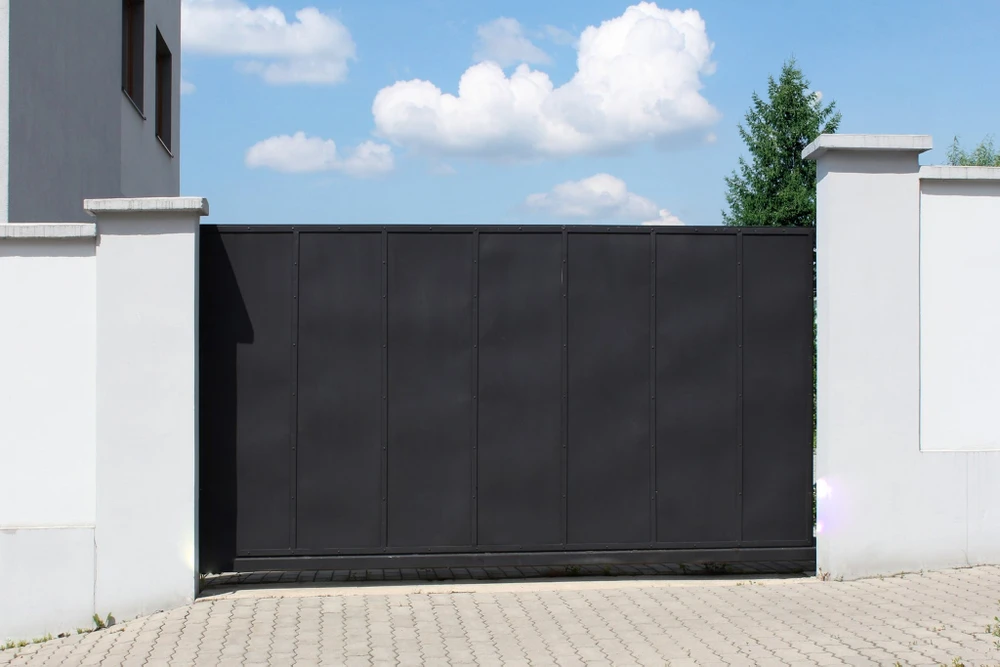 Scène extérieure résidentielle avec portail coulissant noir fermé entre piliers blancs en béton