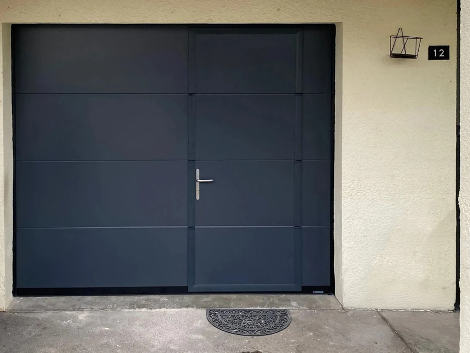 Extérieur résidentiel avec portail de garage sectionnel gris anthracite fermé, intégrant une porte piétonne avec poignée métallique argentée